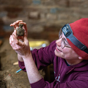 Staff Archaeologist Natalie Reid holds the glass bottle she found in the eastern palisade trench inside the Church Tower.