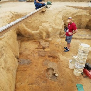 Archaeologists stand in and next to an excavation unit