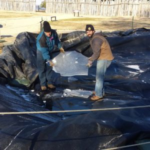 Archaeologists lifting ice sheet from tarp covering excavation unit