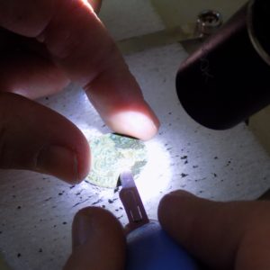 Conservator working on coin under microscope light