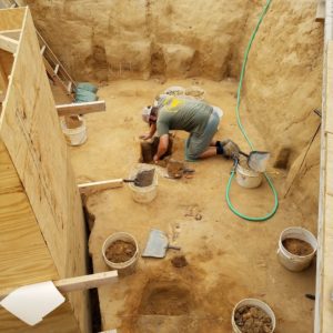 Archaeologist excavating a posthole in a deep unit