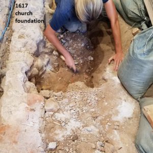 Archaeologist excavates features between foundations and sandbags