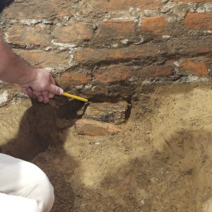 Archaeologist points to metal box buried under brick wall