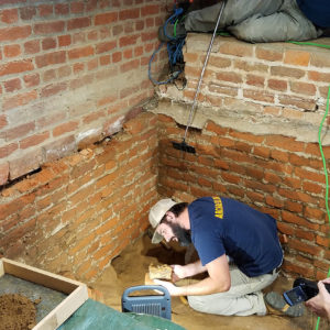 Archaeologist excavating small metal box from under brick wall