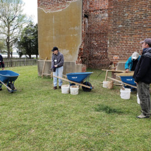 Group standing with wheelbarrows in front of brick ruins
