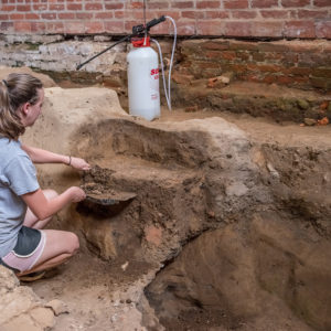 Archaeologist scrapes excavation unit wall with trowel and dustpan