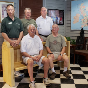 Five men sit on wooden bench inside offices