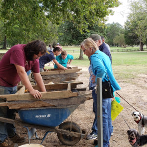 Visitors watch archaeologists screen artifacts over wheelbarrow