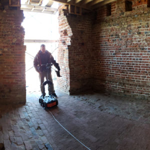 Man pushing a ground penetrating radar unit inside of a brick church tower