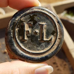 Glass wine bottle seal stamped with the initials "F*L"