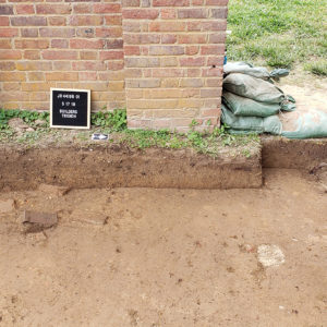 Archaeologist points to excavated feature in front of brick gates