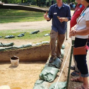 Archaeologist talks to visitors in front of excavation unit