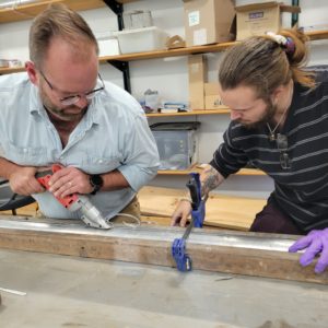 Dr. David Leslie and undergraduate student Preston Senderoff remove portions of the aluminum tube holding the soil sample.