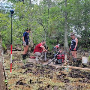 Field school student Annabel Lawton, TerraSearch Geophysical's Dr. David Leslie, field school student Ellie Taylor, and Senior Staff Archaeologist Sean Romo use the vibracore process to take a soil sample of the Pitch and Tar Swamp.