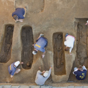 Aerial view of archaeologists excavating four skeletons