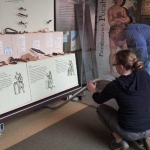 Two staff members vacuum underneath a museum exhibit case of artifacts