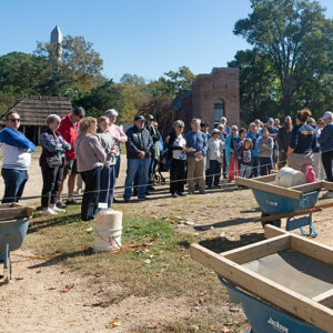 Archaeological Field Technician Hannah Barch describes the 1607 Burial Ground excavations to visitors on an archaeology tour. Archaeological Field Technician Katie Griffith screens for artifacts at left.