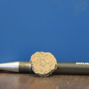 Corroded button next to pen for scale