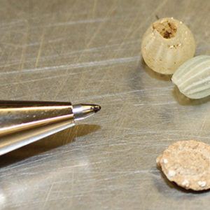Lead rosette and four beads on a lab table next to a pen tip for scale