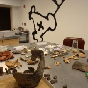 Mended earthenware pot and an assortment of ceramic sherds on a lab table