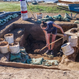 archaeologist shoveling dirt in an excavation unit