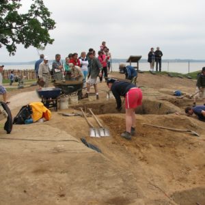 A group of visitors watch archaeologists shoveling dirt in large excavations
