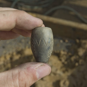 Hand holding a pipe bowl fragment inscribed with the initial W, vertical diamond decorations, and stippling around rim