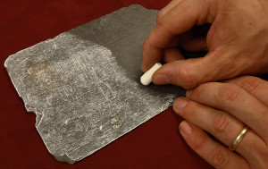 hand rubbing a piece of chalk on an inscribed piece of slate