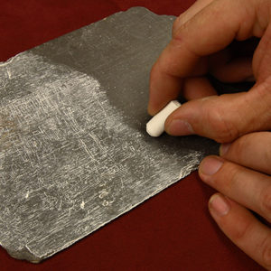 hand rubbing a piece of chalk on an inscribed piece of slate