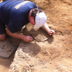 archaeologist using a pick to excavate an artifact