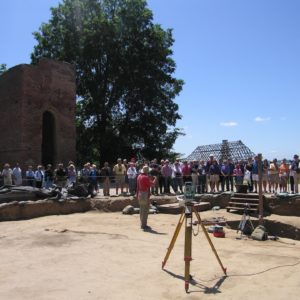 Archaeologist speaks to a large group surrounding excavations