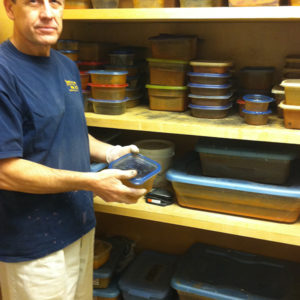 man holding a storage container with artifacts and standing next to shelves lined with an assortment of filled containers