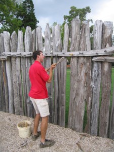 Man hammering a peg into a crosspiece of a wooden palisade