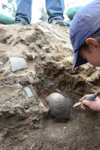 Archaeologist scraping dirt from around a buried clay pot