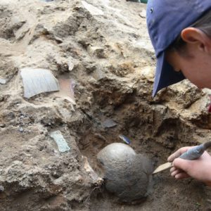 Archaeologist scraping dirt from around a buried clay pot