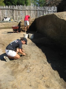 Archaeologist troweling in an excavation unit while another shovels in the background