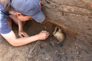 Archaeologist brushing dirt from around a buried earthenware costrel