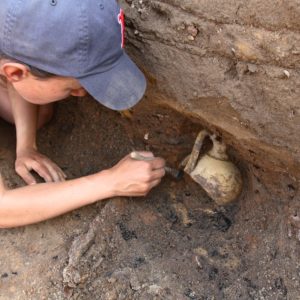 Archaeologist brushing dirt from around a buried earthenware costrel