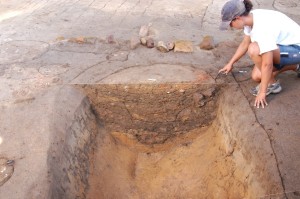 Archaeologist pointing to a bisected ditch showing various stratigraphic layers in the profile