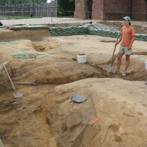 Archaeologist standing with a shovel in a large excavated area in front of a brick church