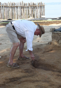 Archaeologist bending over to excavate a feature with a trowel