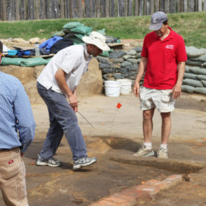Three archaeologists examining excavated brick foundations