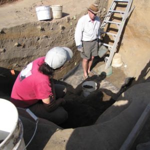 Two archaeologists talk while standing in an excavation unit