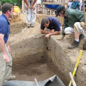 Four archaeologists examining a feature in the corner of an excavation unit