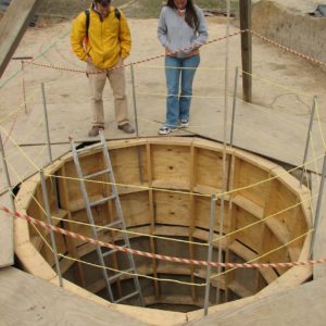 Two archaeologists look down a circular structure into an excavated well