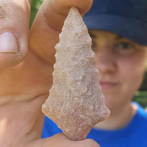 Researcher holding triangular rose-colored quartzite projectile point