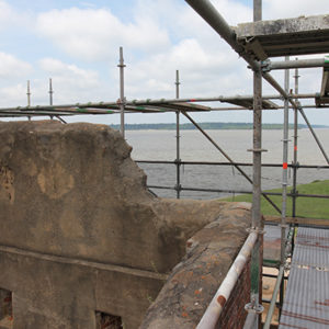 scaffolding around the top of a brick tower looking towards a riverbank