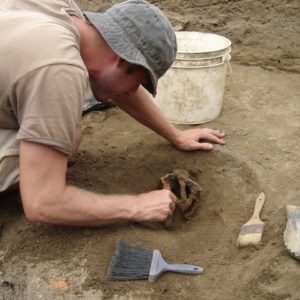 Archaeologist bending over a sword basket hilt in situ