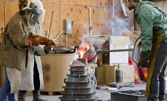 workers in protective gear pouring molten bronze into a mold