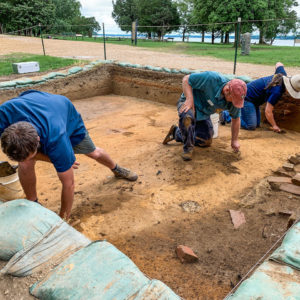 Three archaeologists trowel in excavation unit